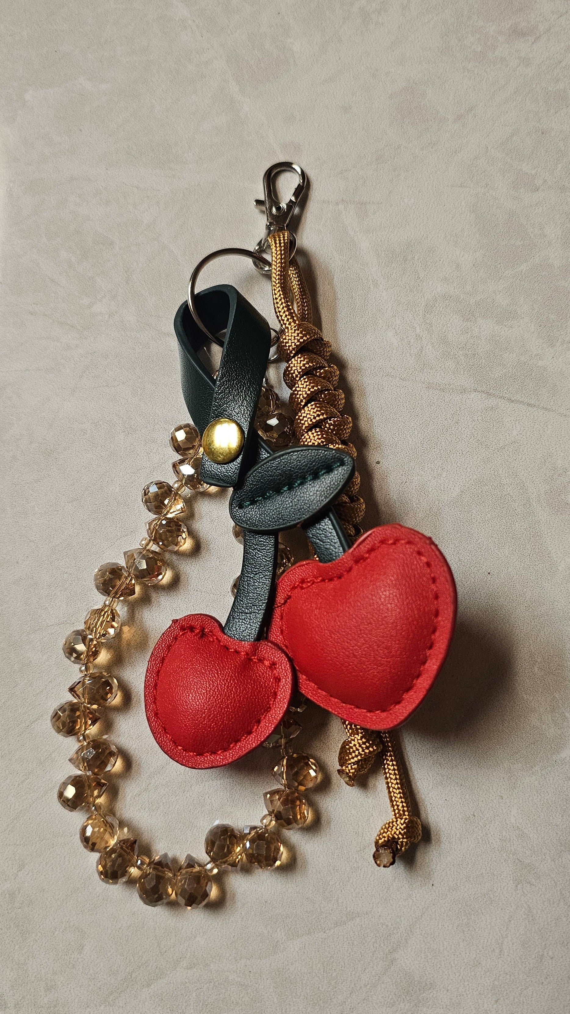 Keychain with stitched cherry and gold beads on a textured surface